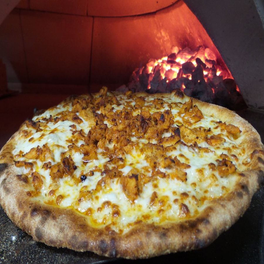 A pizza is sitting in front of a wood fired oven.