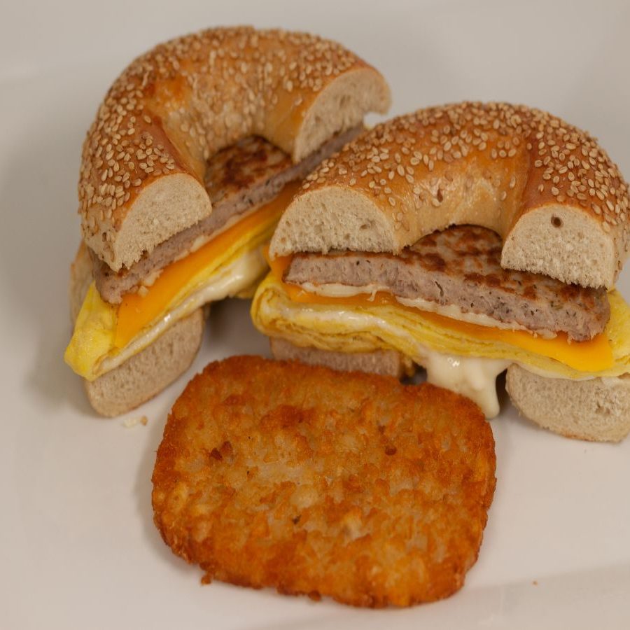 A bagel sandwich with eggs and hash browns on a plate.
